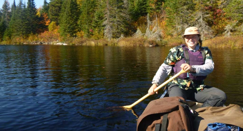 A person sitting in a canoe wearing a lifejacket smiles at the camera